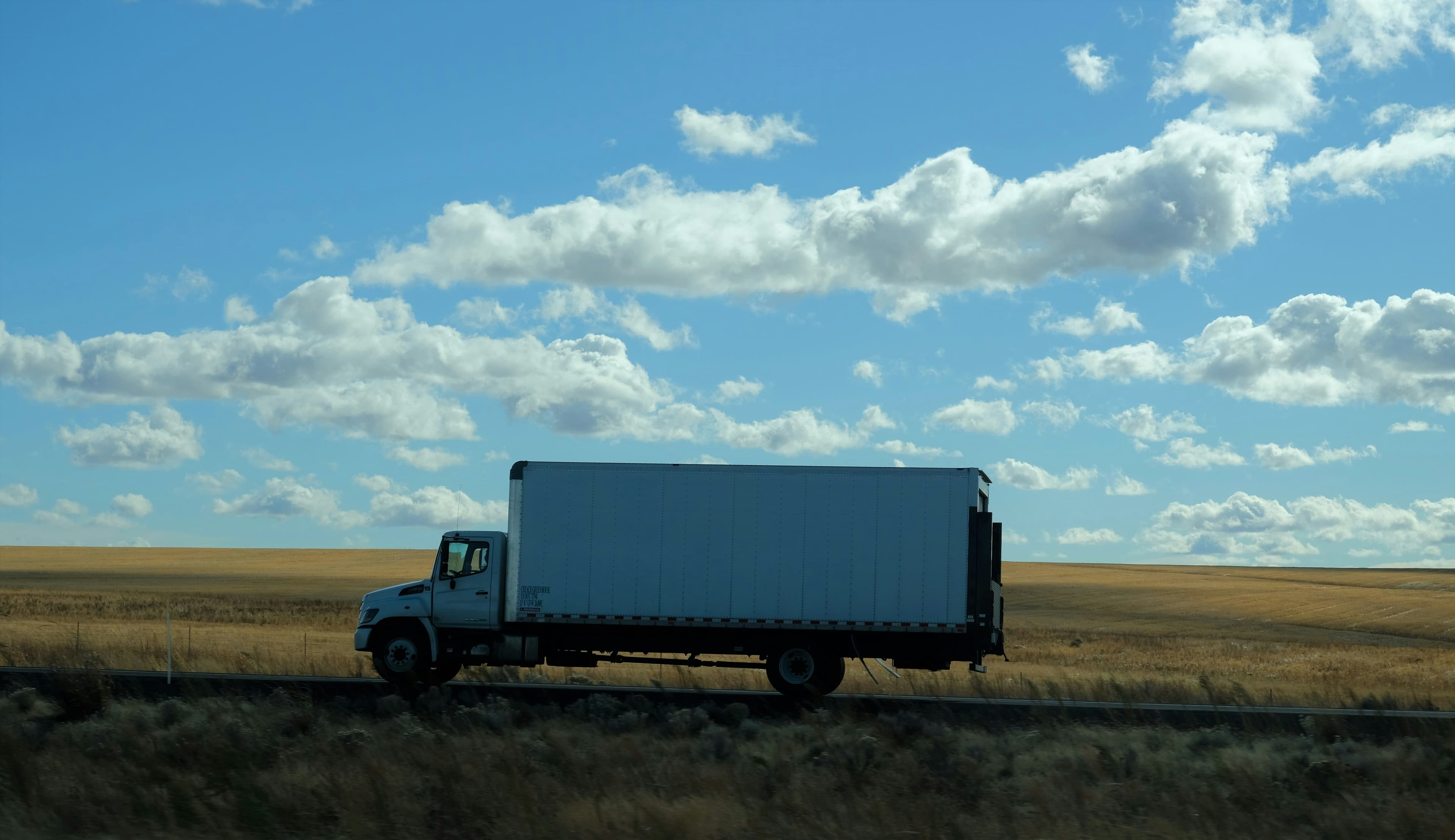 Box truck crossing open prairie under a big sky