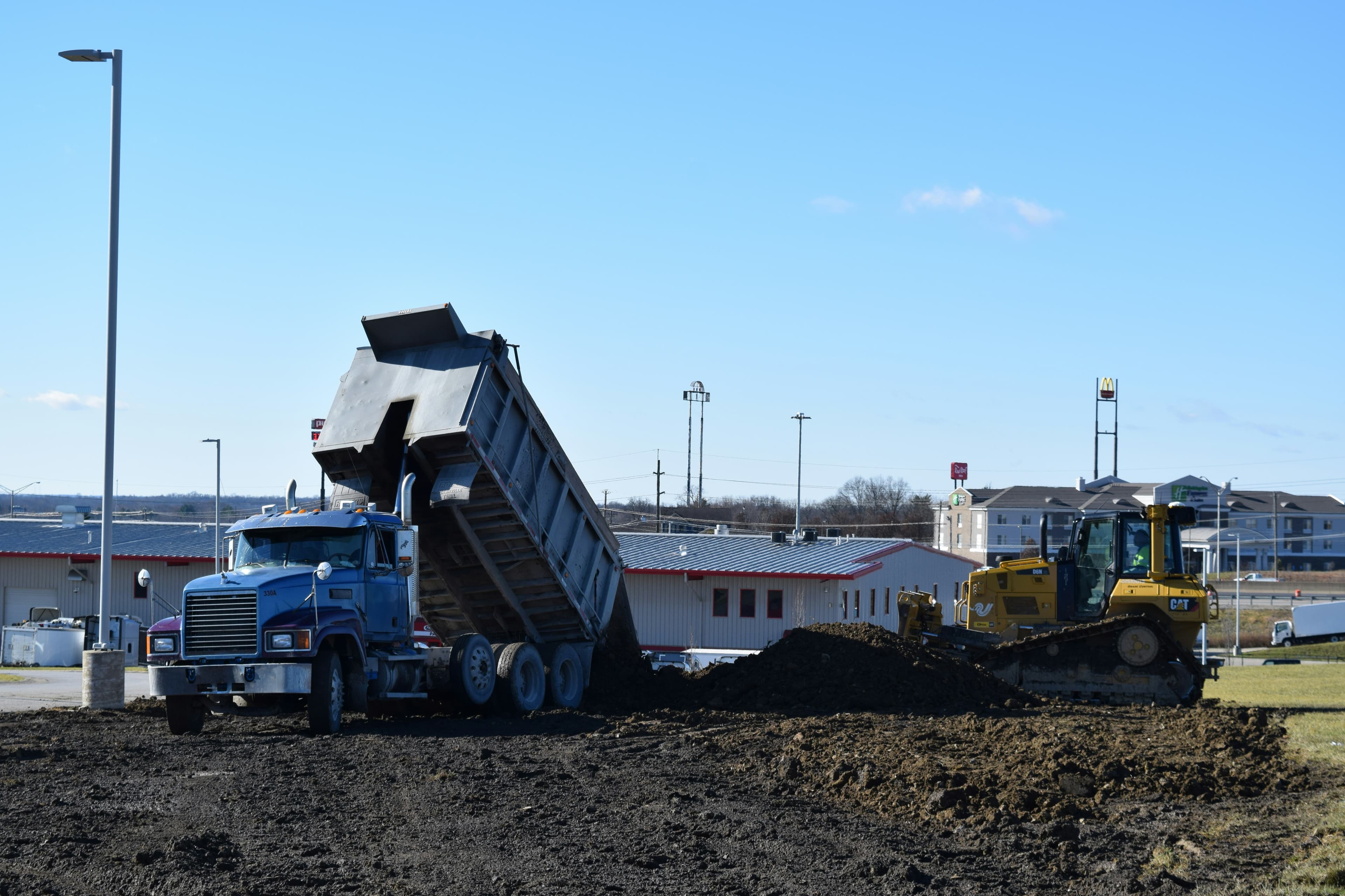 Dump truck tipping a load of dirt beside a bulldozer on a commercial job site