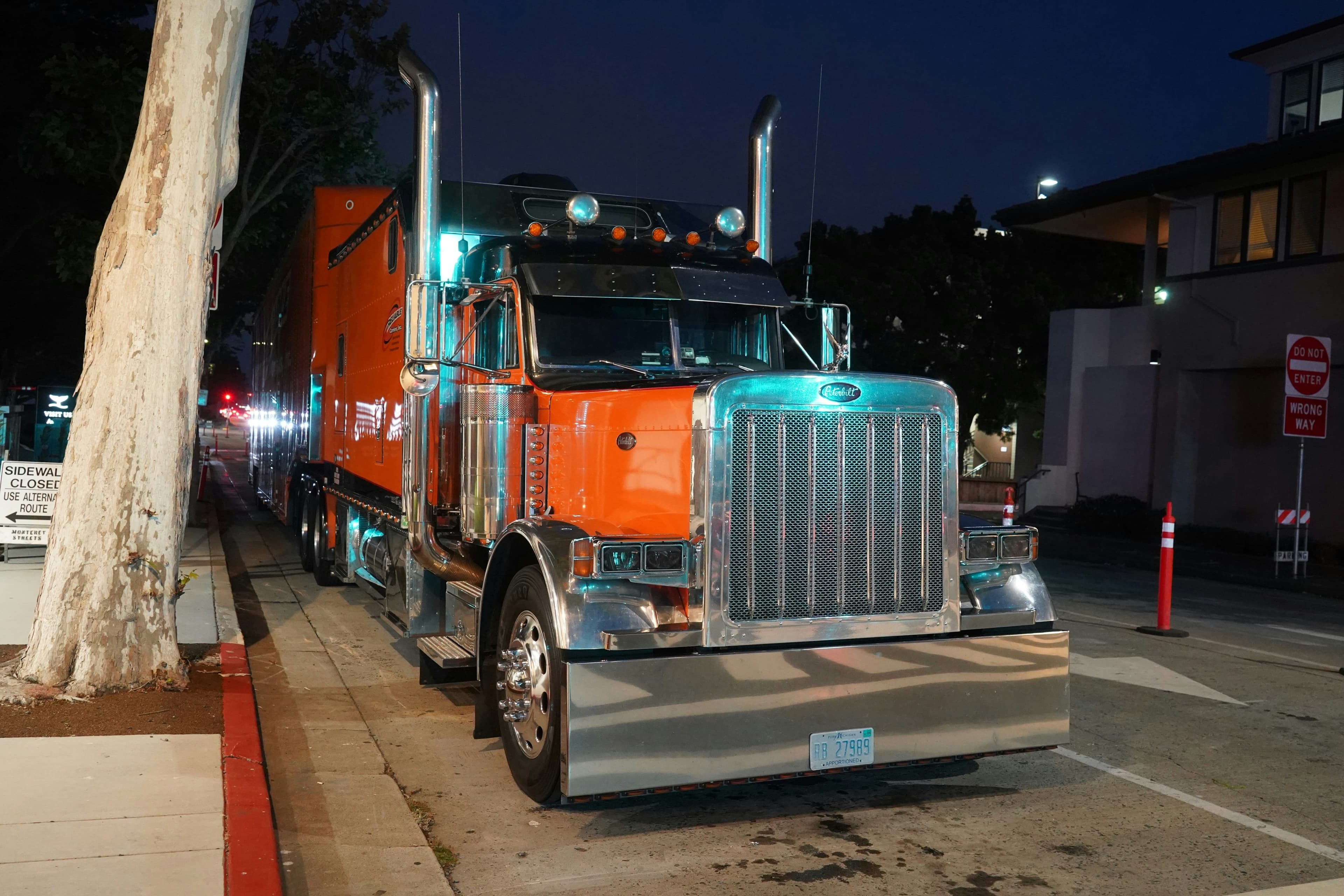 Orange long-nose Peterbilt parked at the curb at night