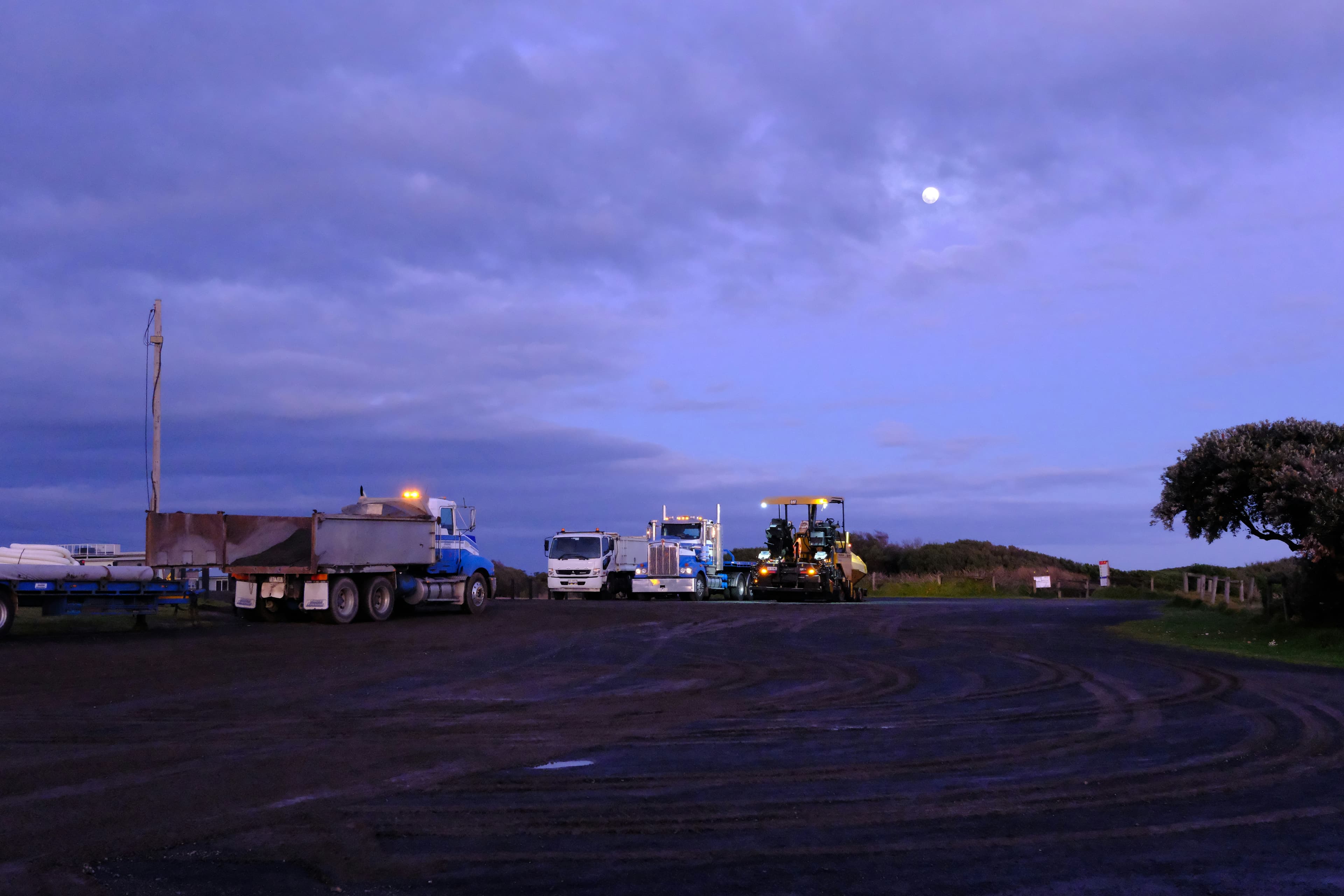 Trucks parked for the night in a gravel lot under a dusk sky and moon