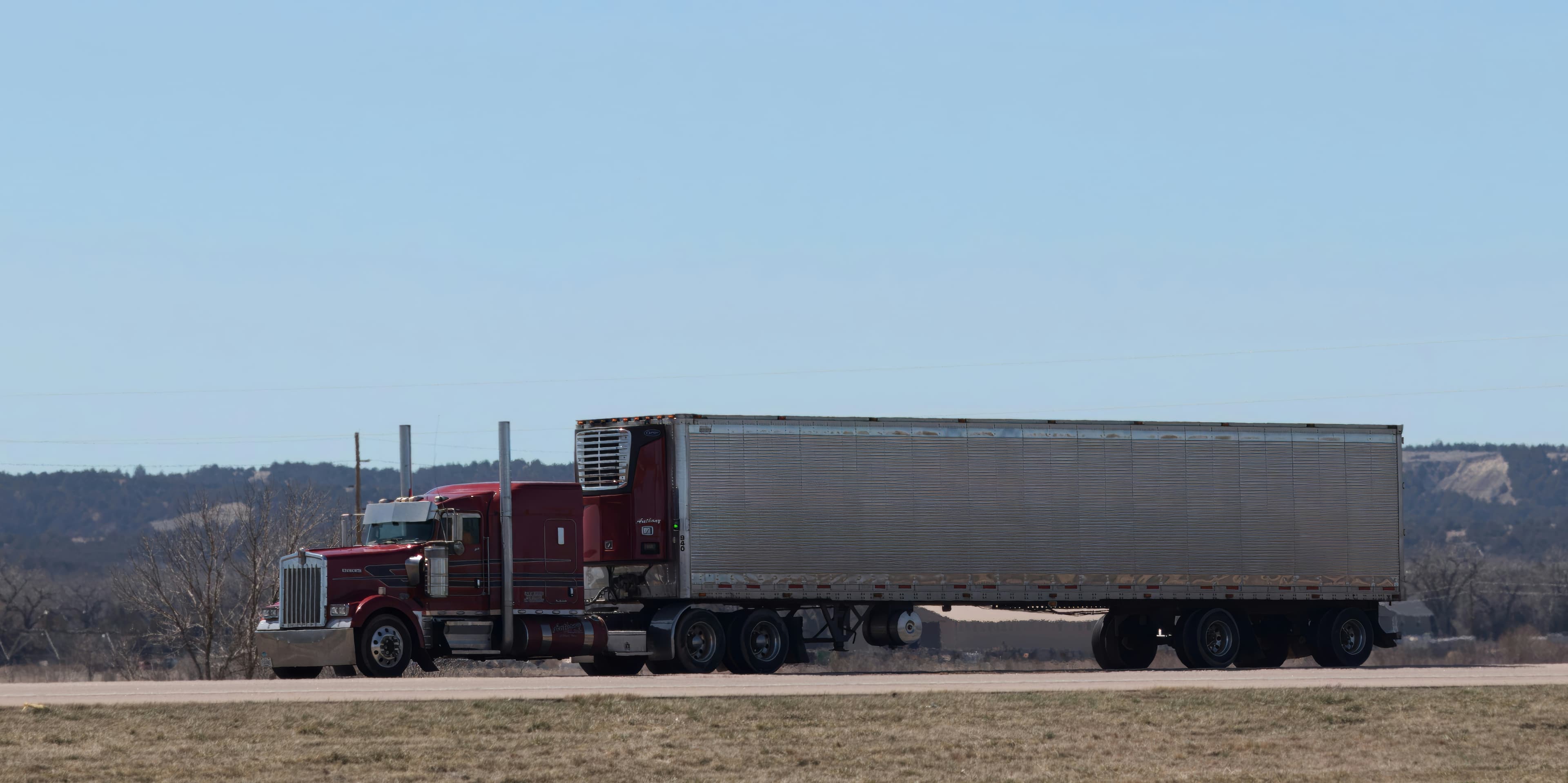 Long-nose tractor pulling a refrigerated trailer across open rangeland