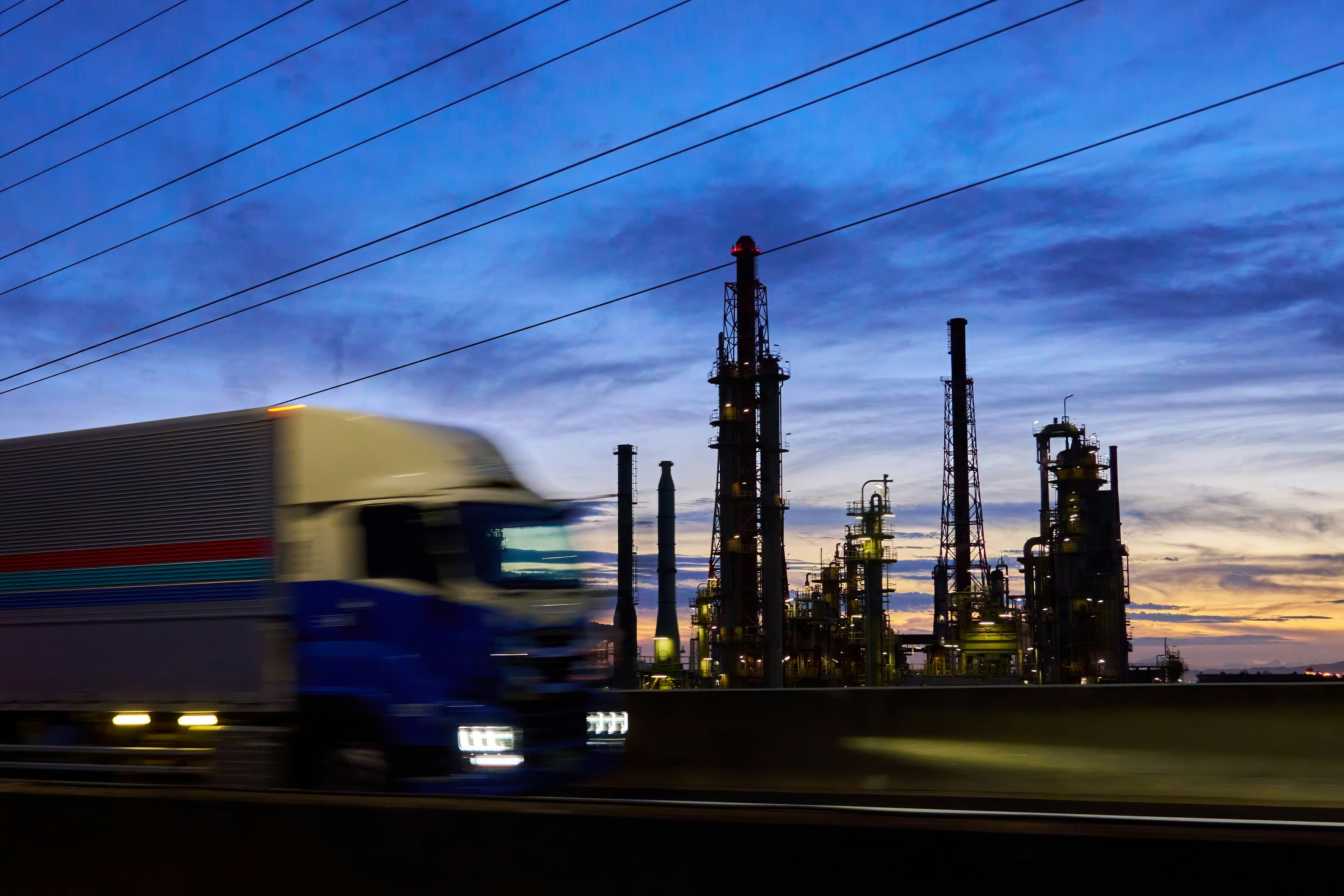 Tractor-trailer passing a refinery at dusk