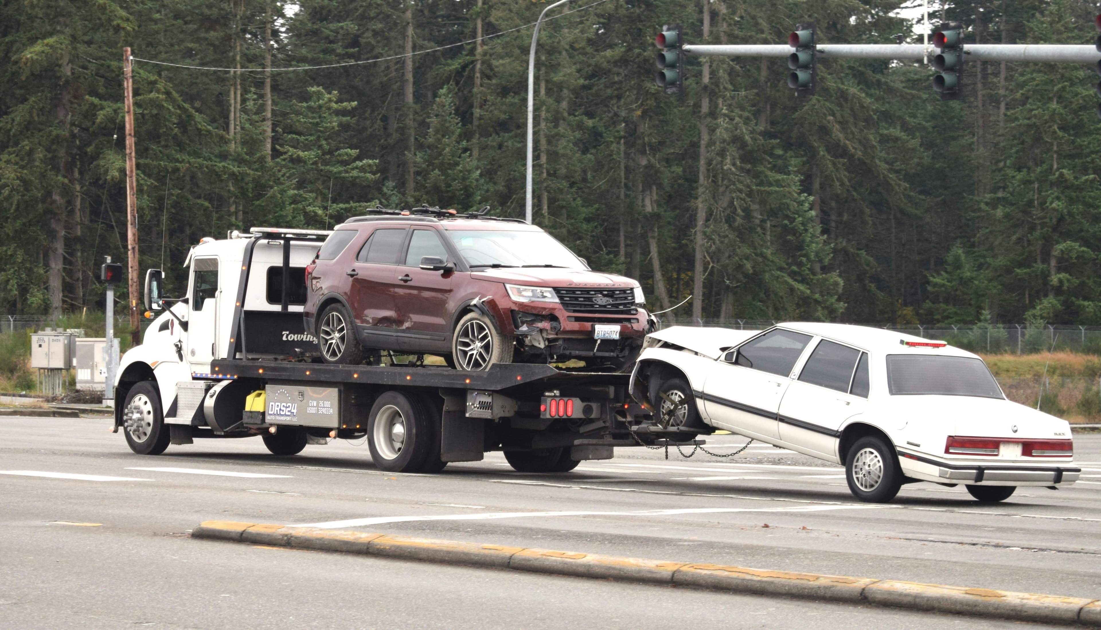 Rollback tow truck carrying an SUV while towing a damaged sedan